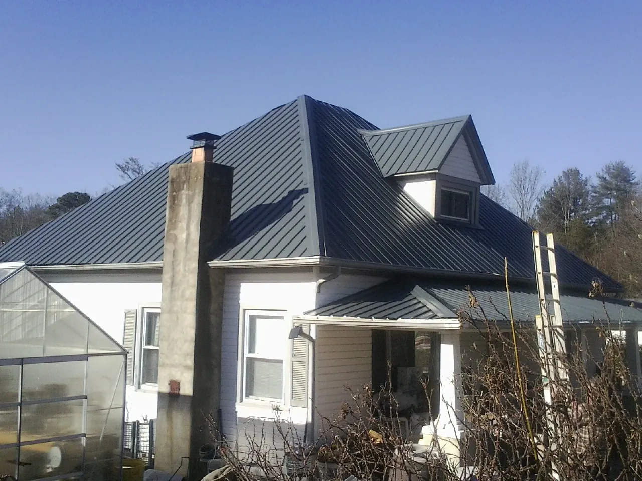 Dark blue standing seam metal roof on a white farmhouse with dormer — Slate & Tile Roof Repair by Roofing Brothers in Bluff City