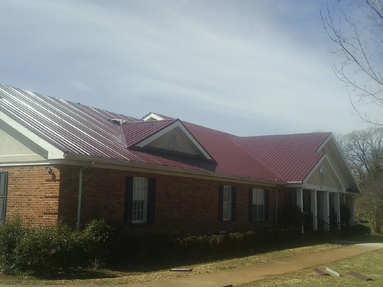 Red metal roof with gabled entries on a long brick building, from a Hail Damage Roof Repair job in Bluff City