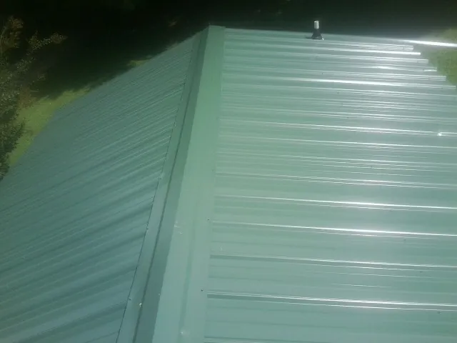 New green metal panels meeting at the ridge of a roof — Flat Roof Repair work by our crew in Bluff City
