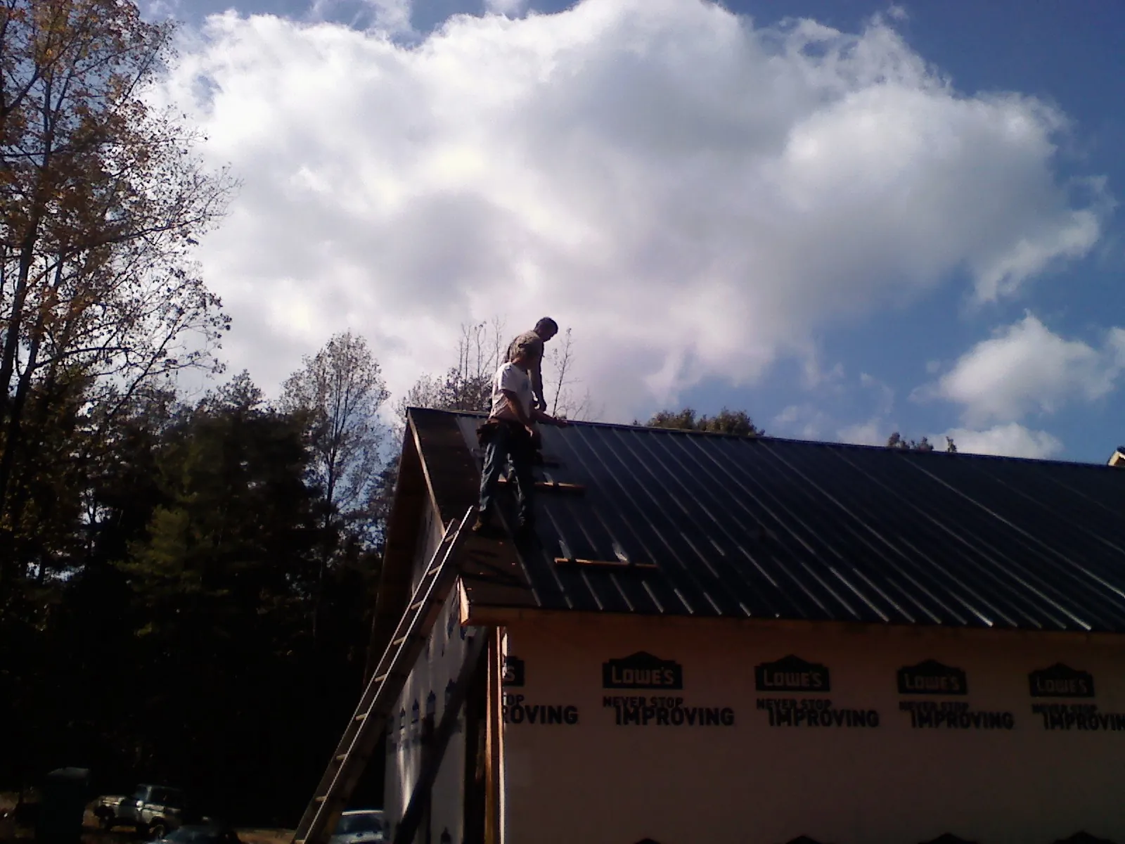 Roofer fastening dark metal panels high against a cloudy sky, from a Roof Inspection job in Bluff City