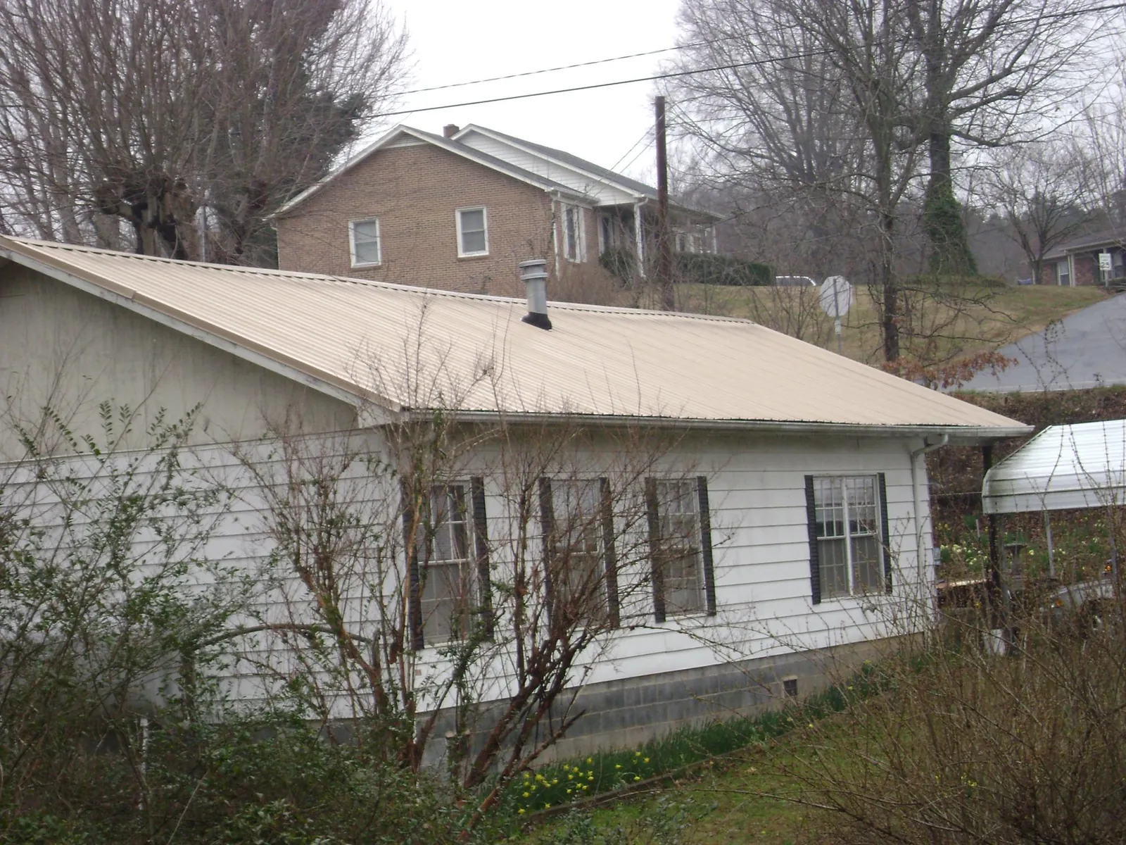 Tan metal roof on a white sided house set into a hillside — Commercial Roofing by Roofing Brothers in Bluff City