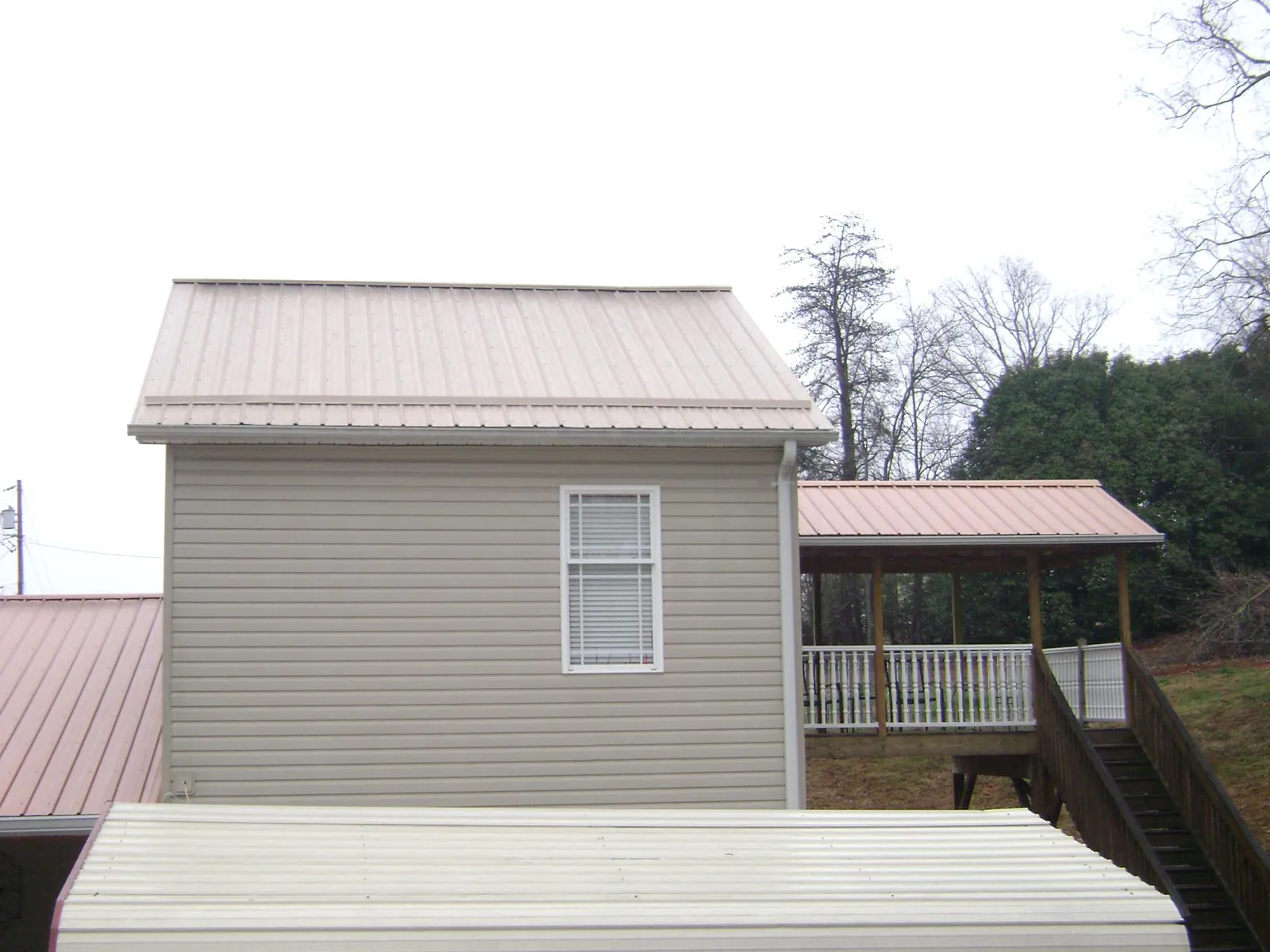 Tan metal roofs on a two story addition and attached porch, from a Roof Replacement job in Bluff City
